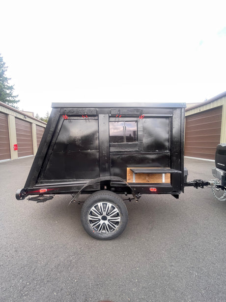 This black, custom-built camping trailer, ideal for unique rv rental experiences, features a window and outdoor shelf.