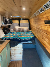 Step inside this inviting RV rental: a wood-paneled camper interior with a cozy bed, sofa, and small kitchen.