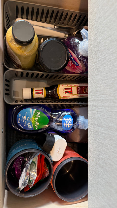 Organized kitchen supplies in an RV rental drawer: condiments, hand soap, dish soap, and travel mugs neatly stored.