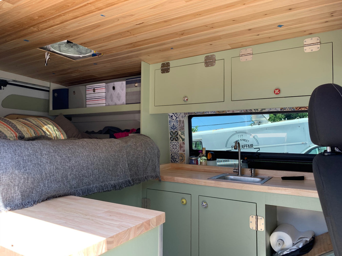 This RV rental offers a compact kitchen with a sink, comfortable bed, overhead storage, and a light wood ceiling. — photo 2