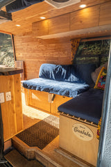 Cozy rv rental van with warm wood interior, blue cushions, custom built-ins, and a "Gualala" name sign.