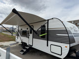 Open Range RV rental: A white & grey travel trailer with an extended awning, parked outside on a cloudy day.