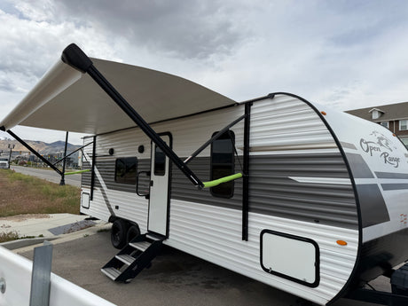 Open Range RV rental: A white & grey travel trailer with an extended awning, parked outside on a cloudy day.