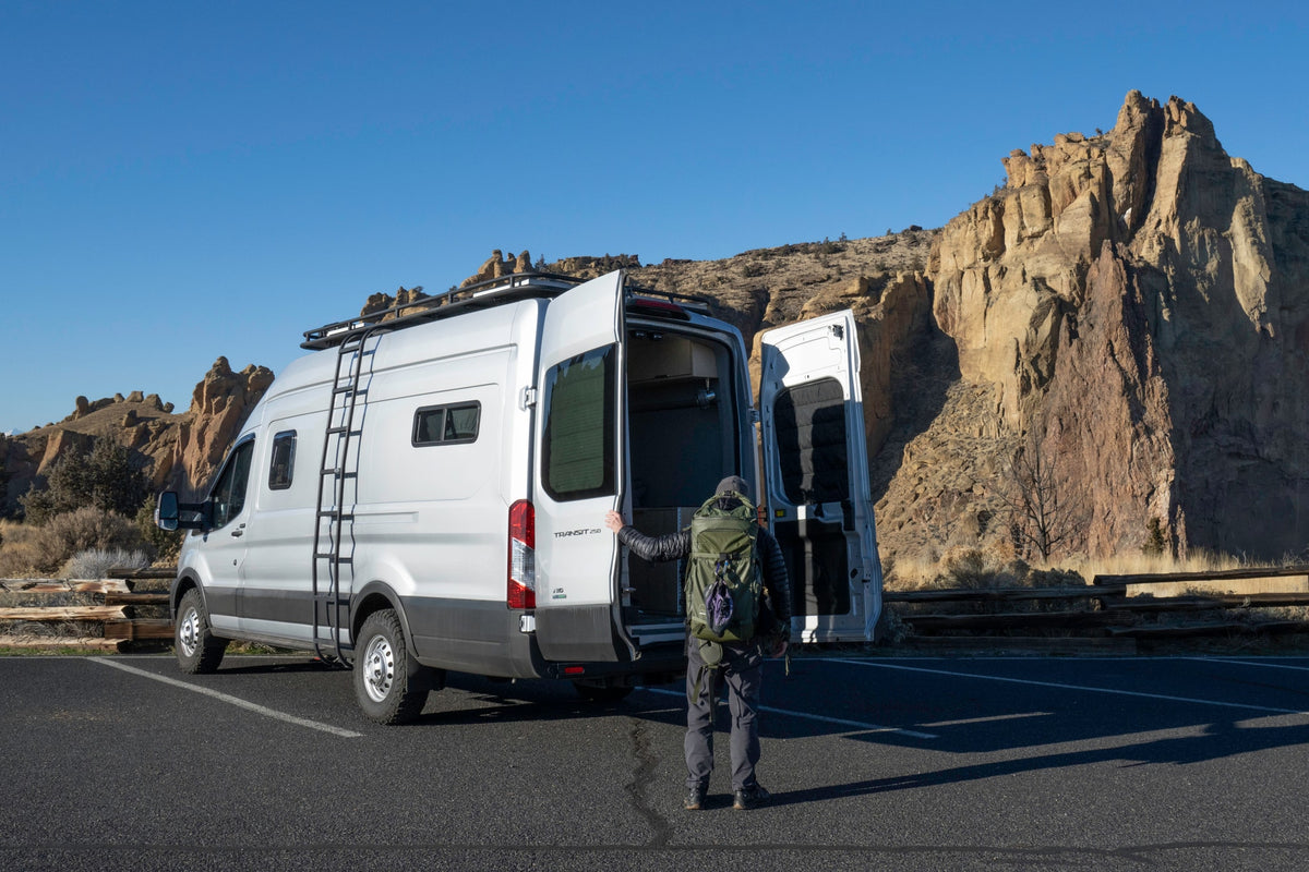 Adventure beckons! A person by an open silver Transit camper van at rocky cliffs. Ideal rv rental for exploration.