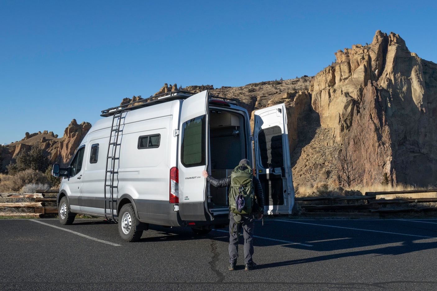 Adventure beckons! A person by an open silver Transit camper van at rocky cliffs. Ideal rv rental for exploration.