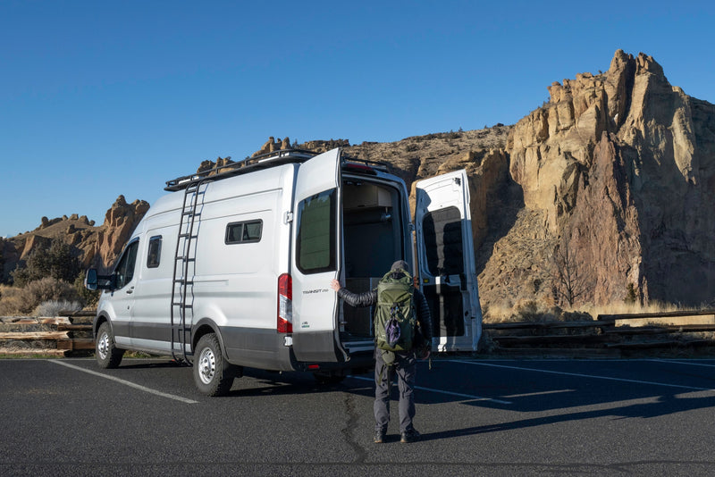 Adventure beckons! A person by an open silver Transit camper van at rocky cliffs. Ideal rv rental for exploration. — photo 1