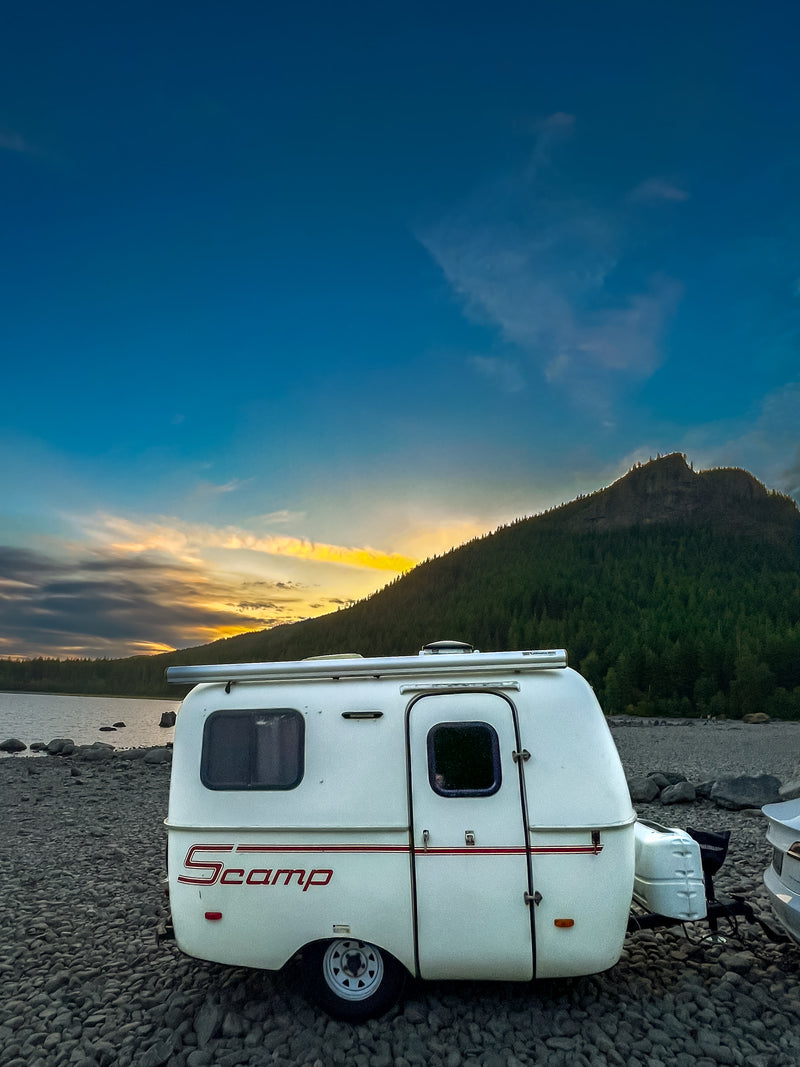 Experience the beauty of nature with an RV rental! This white Scamp camper sits by a lake at sunset, framed by a forested mountain. — photo 6