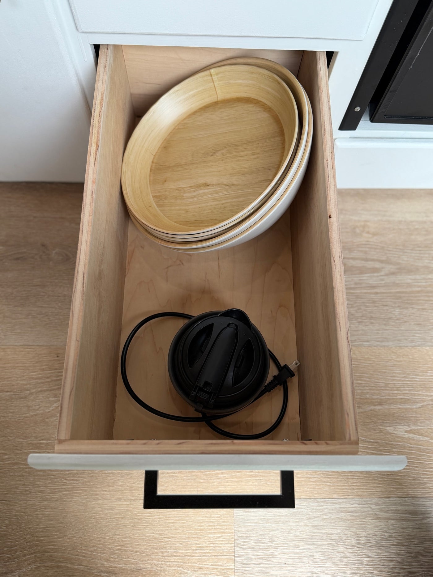 This RV rental's kitchen drawer is open, revealing stacked wooden bowls & a compact black electric appliance for convenient storage. — photo 13