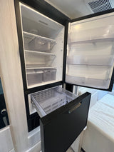 Open compact RV rental fridge and freezer drawer showing interior storage, shelves, and bins.