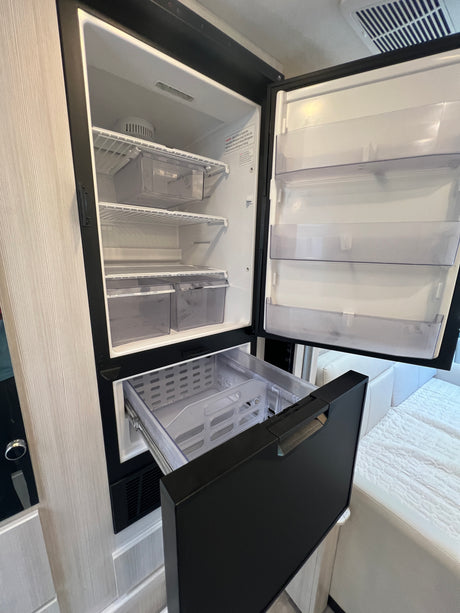 Open compact RV rental fridge and freezer drawer showing interior storage, shelves, and bins.