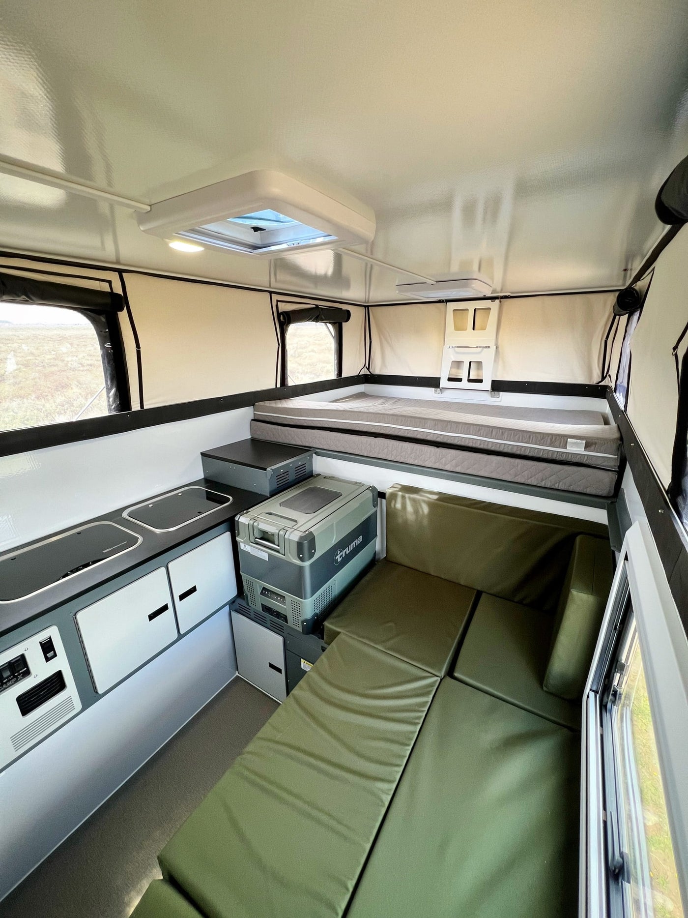 Cozy RV rental interior with elevated bed, kitchen, seating, and portable fridge, perfect for adventures. — photo 5