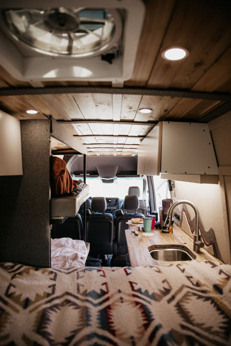 RV rental: Inside a modern camper van showing kitchen, bed, and front seats. Ideal for mobile living.
