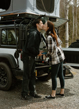A couple kissing beside their adventure rv rental, equipped with a rooftop tent and camp kitchen setup.