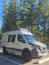 Silver Mercedes-Benz Sprinter camper van parked among tall trees. Ready for your next RV rental adventure!