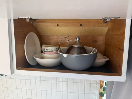 RV rental kitchen: compact cabinet storage with stacked plates, bowls, a colander, and a teapot.