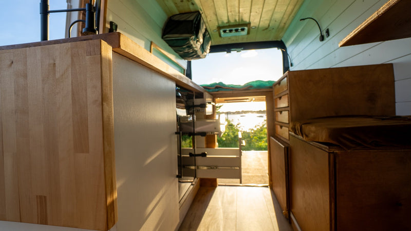 RV rental: Bright camper van interior shows kitchen, pull-out storage, and a scenic lake view from the open rear doors. — photo 18