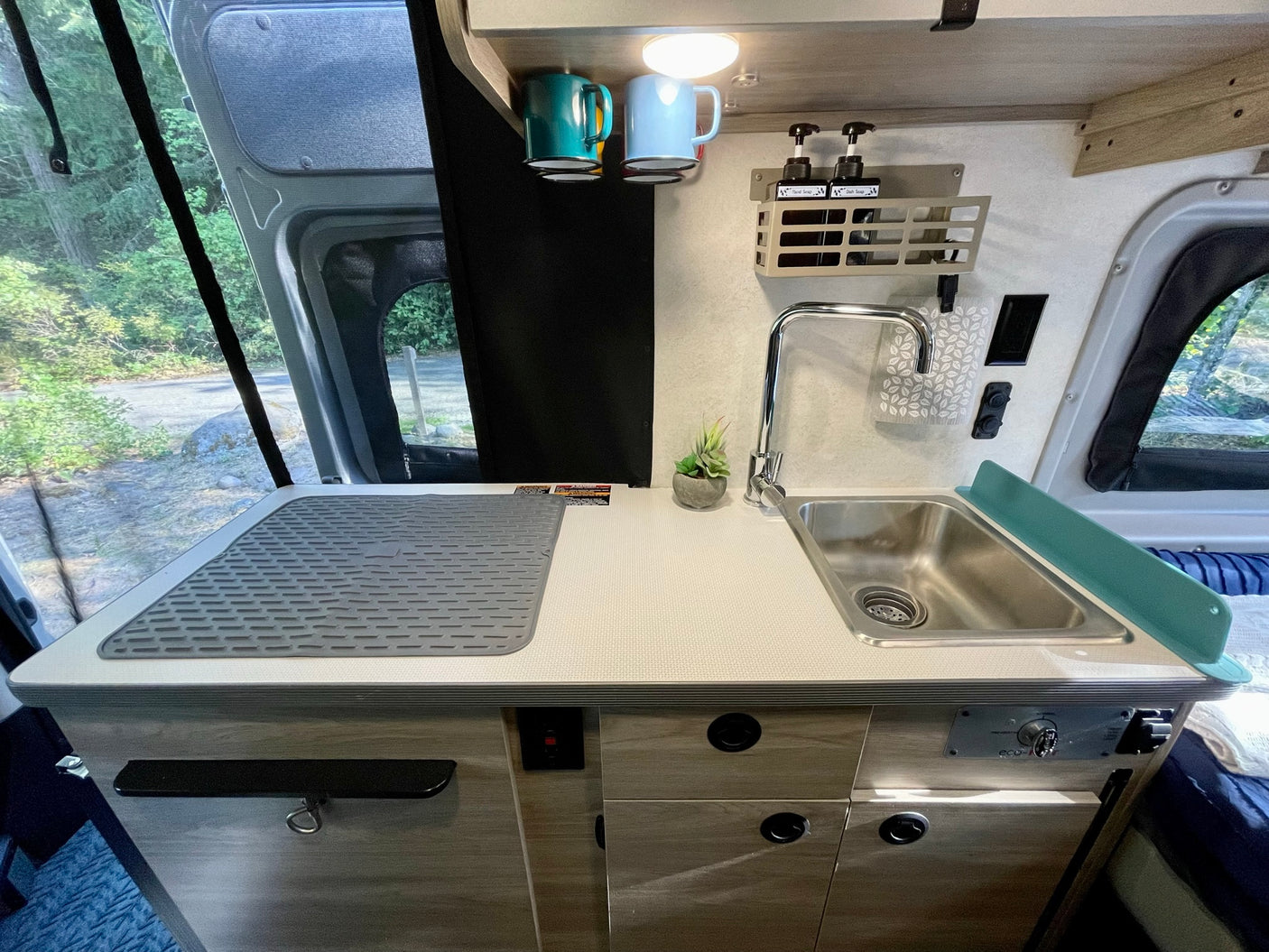 RV rental kitchen: a compact, modern interior with a stainless steel sink, wood-look cabinets, and a serene outdoor view.