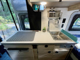 RV rental kitchen: a compact, modern interior with a stainless steel sink, wood-look cabinets, and a serene outdoor view.