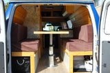 RV rental: View inside a camper van's converted living space with two cushioned benches, a central table, and under-seat storage.