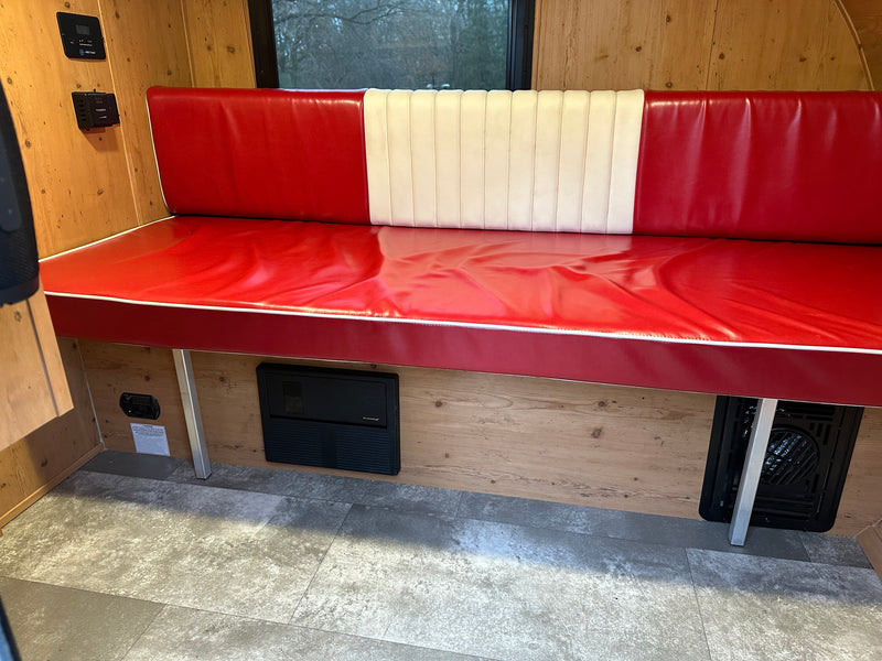 RV rental: Bright red & white dinette bench seating in a wood-paneled interior, with controls & a floor vent. — photo 6