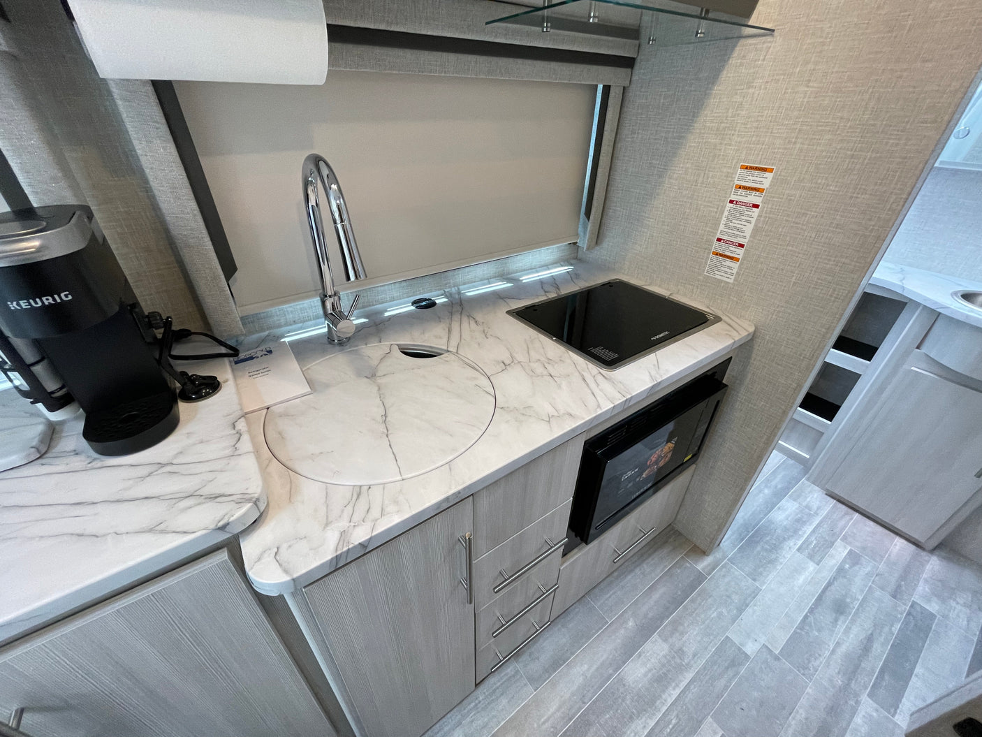 Compact RV rental kitchen featuring a Keurig, covered sink, Dometic cooktop, and microwave on marble-look counters.