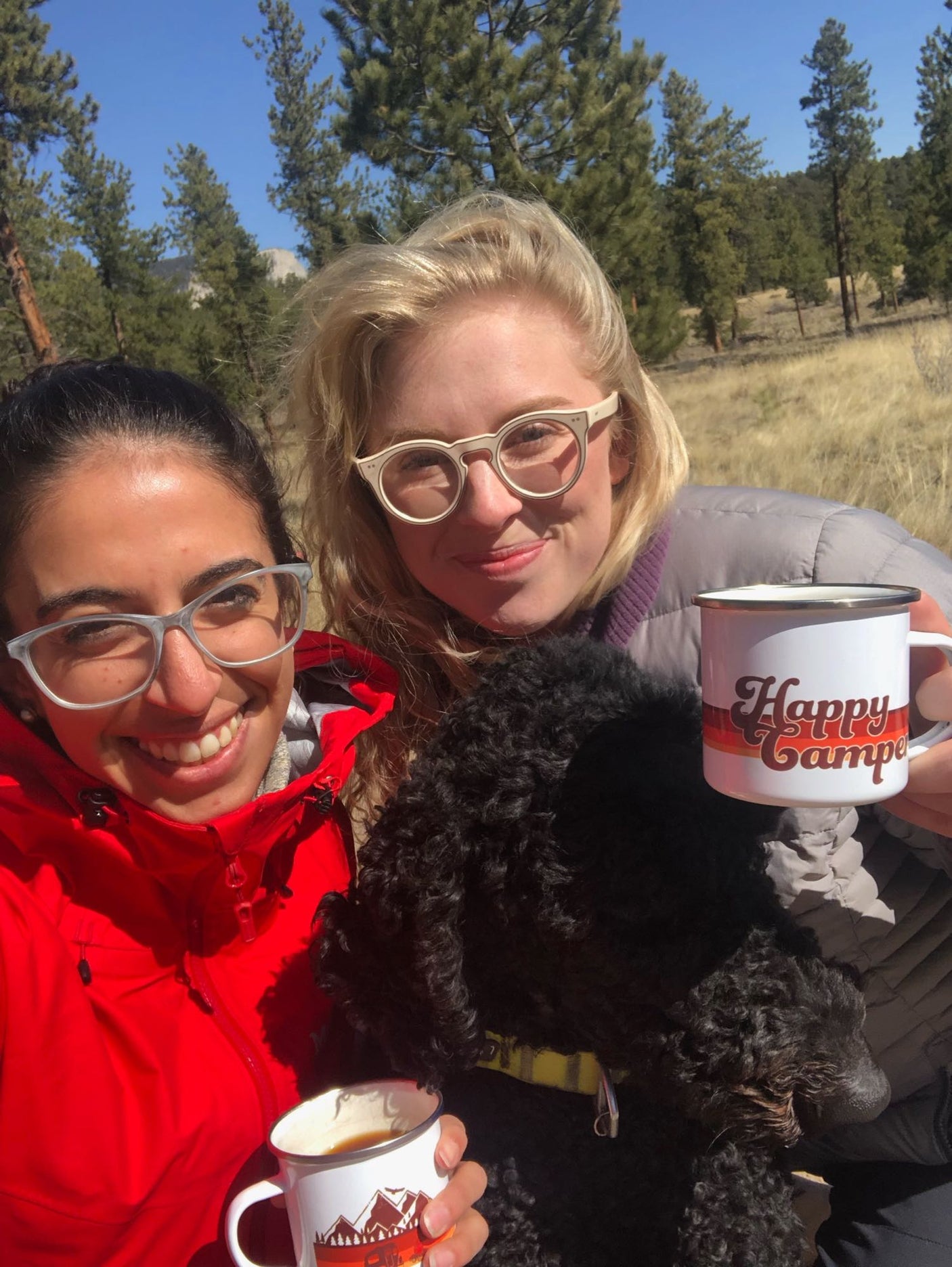 Two women and their dog share coffee mugs in a sunny outdoor setting. Ideal for an RV rental getaway!