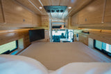 This RV rental features a cozy interior: a spacious bed, TV, compact kitchen, and overhead wood cabinets. Ideal for road trips.