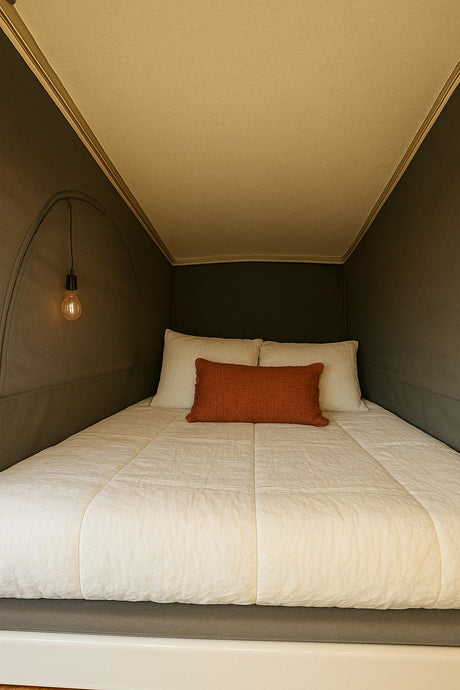 Cozy RV rental sleeping area with soft white bedding, an orange accent pillow, and a warm hanging light.