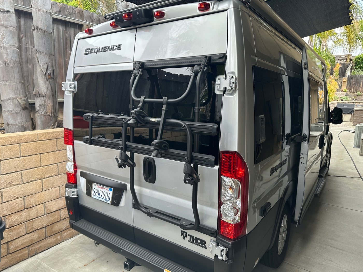 Rear of a silver Thor Sequence camper van with a Thule bike rack, perfect for your next RV rental trip. Doors ajar. — photo 8