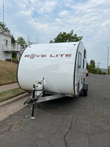 White Rove Lite compact travel trailer, equipped with a propane tank, parked on an asphalt street. Great for RV rental!