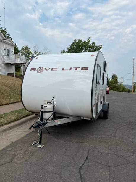 White Rove Lite compact travel trailer, equipped with a propane tank, parked on an asphalt street. Great for RV rental!