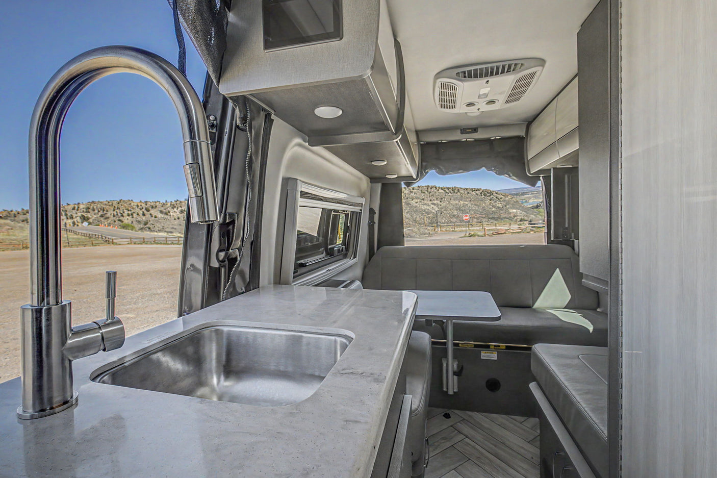 Modern rv rental interior: kitchen with a large sink, sleek countertop, and comfortable dining area with outdoor views.