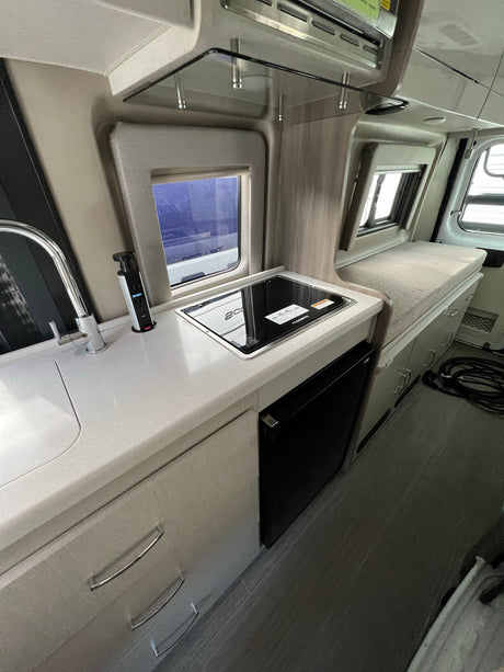 Experience an RV rental: Clean kitchenette with sink, cooktop, and fridge, integrated seating for convenience.