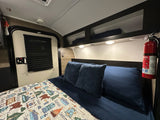 Cozy RV rental bedroom with a bed, camping quilt, and mounted fire extinguisher for safety and comfort.