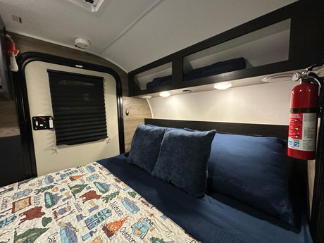 Cozy RV rental bedroom with a bed, camping quilt, and mounted fire extinguisher for safety and comfort.