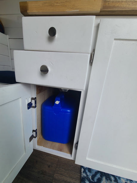 RV rental interior with white cabinets, two drawers, and a visible blue portable water tank, optimizing compact storage.