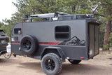 Gray off-road teardrop camper with solar panels, ideal for an rv rental adventure. Parked in a forest setting.