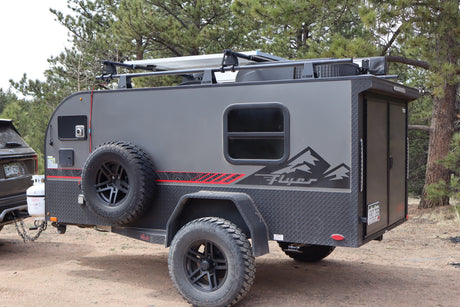 Gray off-road teardrop camper with solar panels, ideal for an rv rental adventure. Parked in a forest setting.