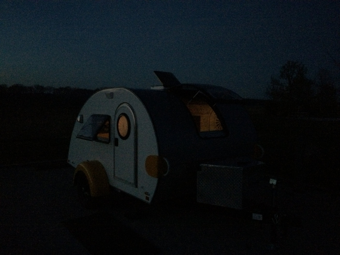 Cozy teardrop camper at night, with warm interior lights glowing. Perfect for your next RV rental adventure.