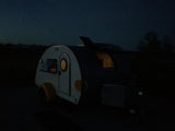 Cozy teardrop camper at night, with warm interior lights glowing. Perfect for your next RV rental adventure.