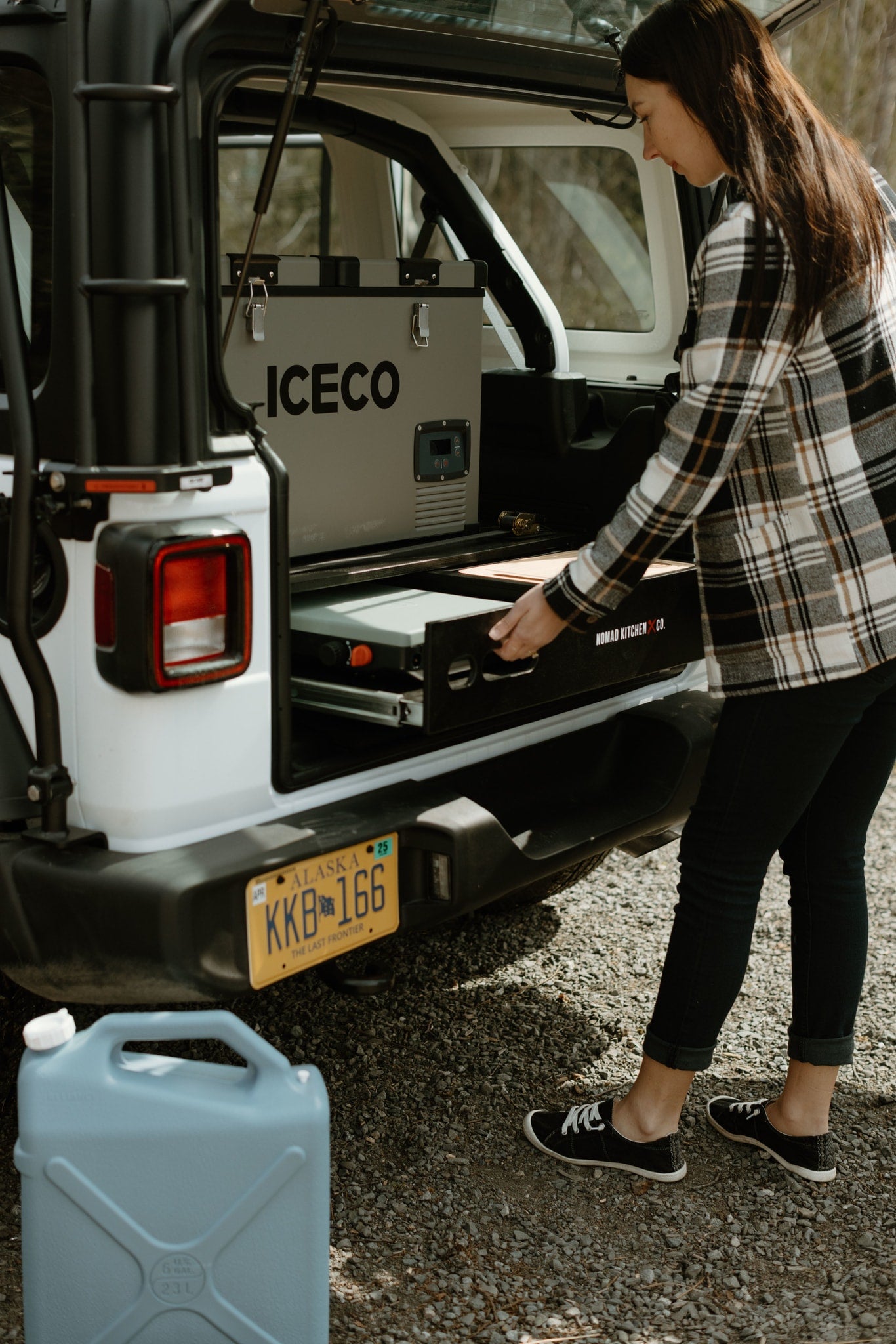 Woman pulls out Nomad Kitchen from rv rental, with ICECO fridge inside. Ready for camping in Alaska.