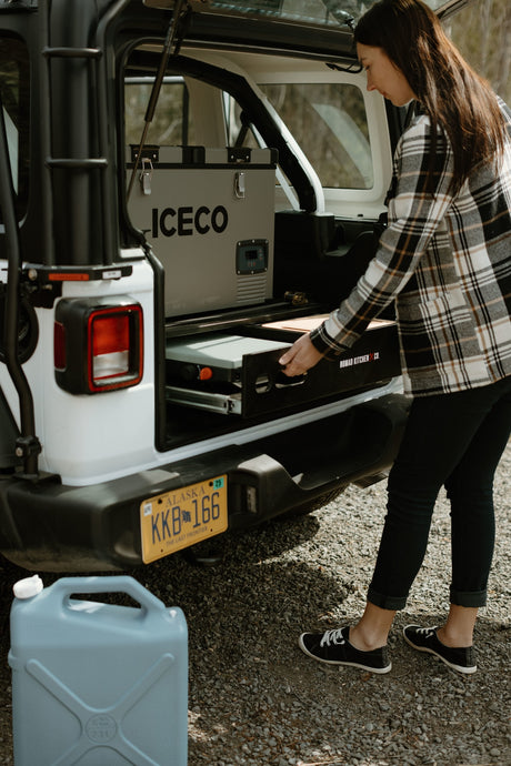Woman pulls out Nomad Kitchen from rv rental, with ICECO fridge inside. Ready for camping in Alaska.