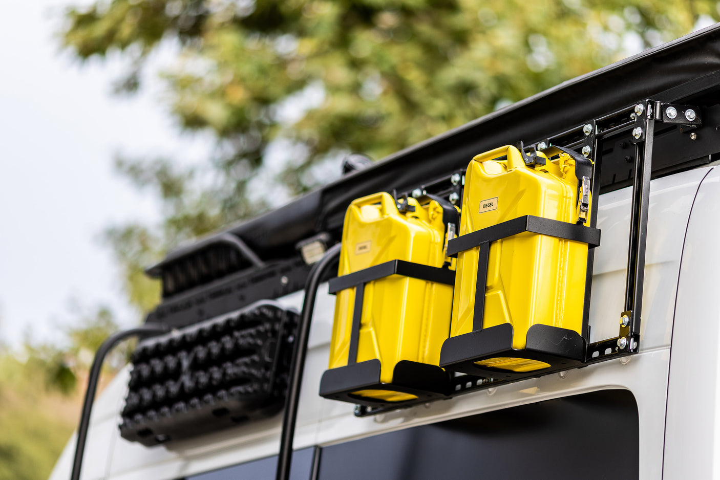 RV rental equipped: Two bright yellow diesel jerry cans & black recovery boards on a white van, ready for adventure.
