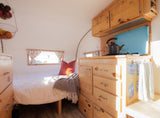 Cozy RV rental interior with bed, built-in wooden storage, and kitchen area. Bright and inviting.
