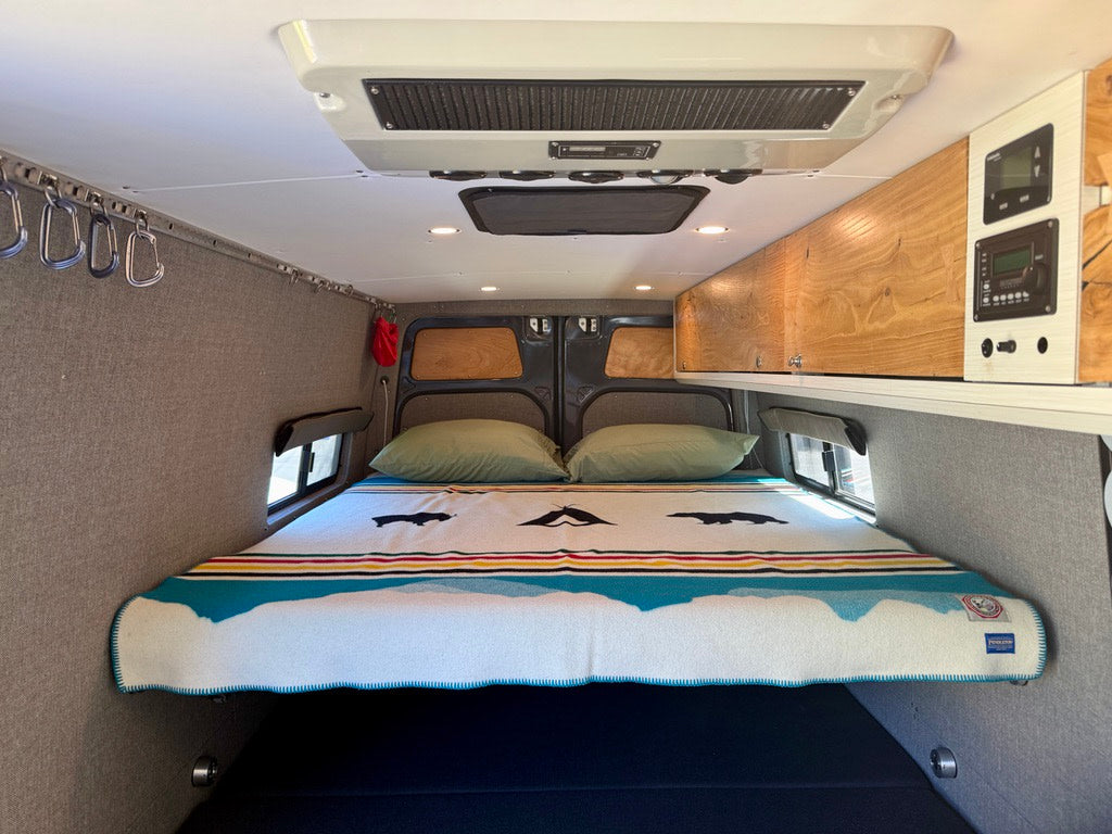 Cozy RV rental interior featuring a comfortable bed, overhead storage, and climate controls. Perfect for adventure!