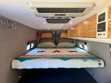 Cozy RV rental interior featuring a comfortable bed, overhead storage, and climate controls. Perfect for adventure!