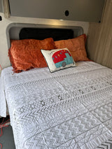 Cozy RV rental bed with a white geometric quilt, plush orange pillows, and a decorative camper cushion.
