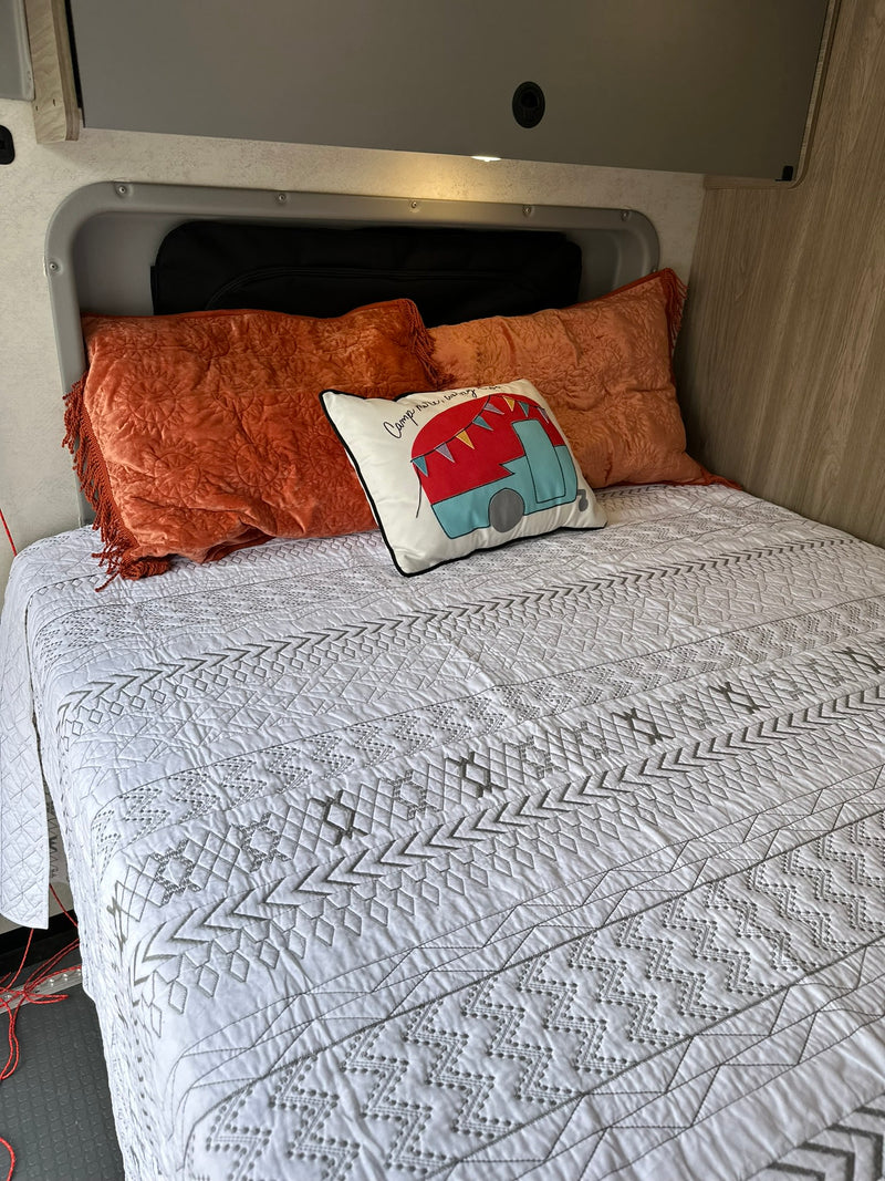 Cozy RV rental bed with a white geometric quilt, plush orange pillows, and a decorative camper cushion. — photo 5