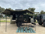 This rugged overlanding trailer, ideal for rv rental, offers an outdoor kitchen, fridge, and large awning, hitched to an off-road Jeep.