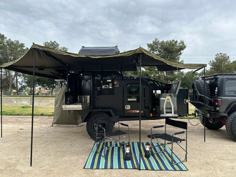This rugged overlanding trailer, ideal for rv rental, offers an outdoor kitchen, fridge, and large awning, hitched to an off-road Jeep.
